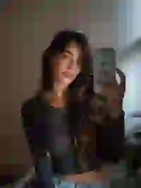 woman-in-black-top Portrait of a woman in black long sleeve crop top taking selfie with a white iPhone in a bedroom. Template for Undress AI.