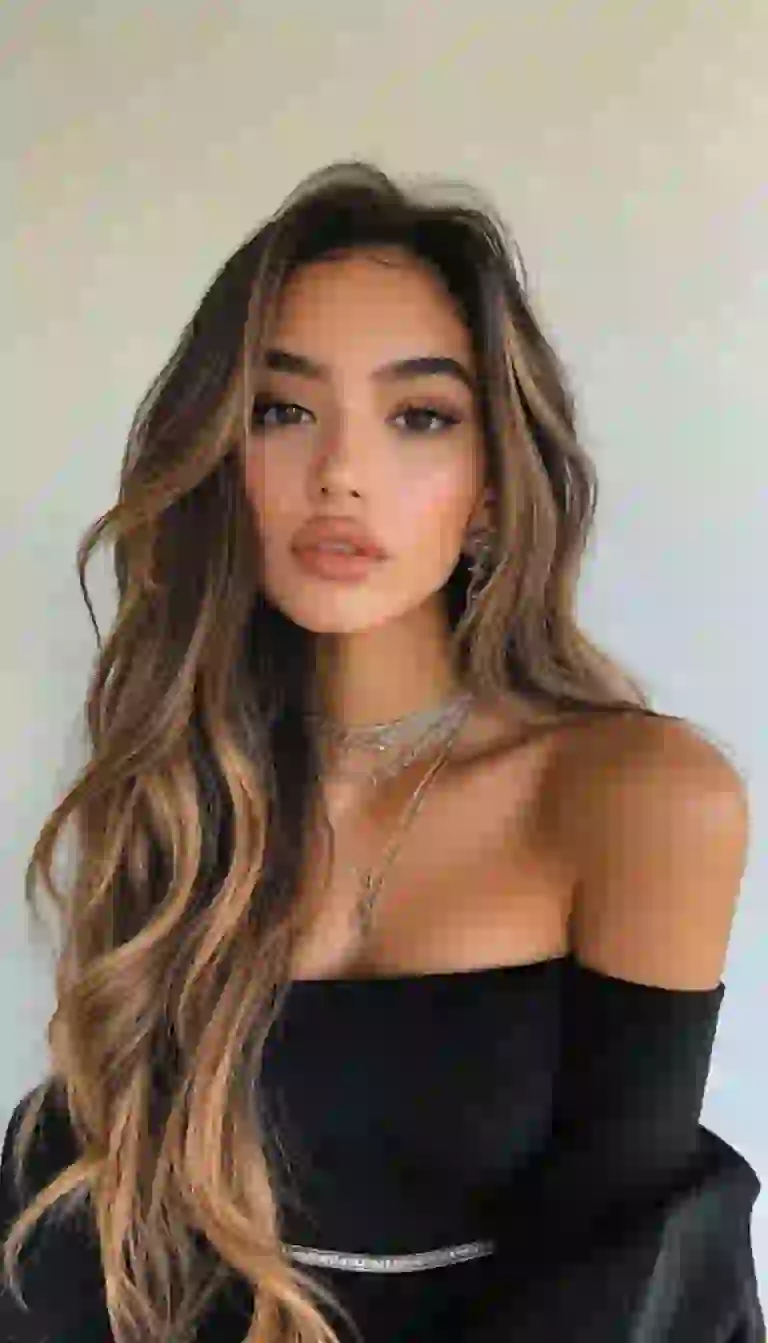 Sexy woman with tanned skin in black off-the-shoulder dress posing indoors.